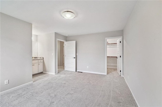 unfurnished bedroom with a walk in closet, light colored carpet, ensuite bath, and baseboards