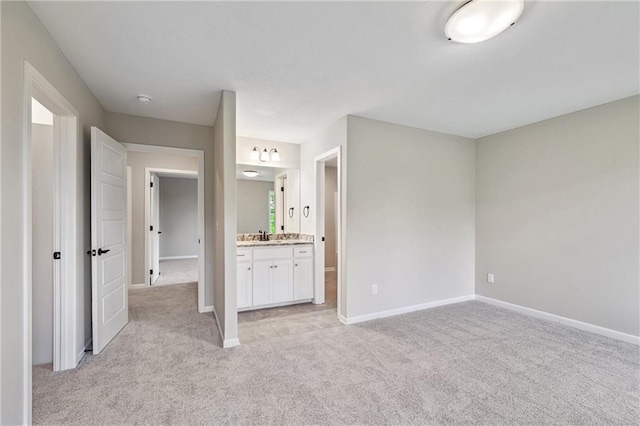 unfurnished bedroom featuring light carpet, ensuite bathroom, a sink, and baseboards