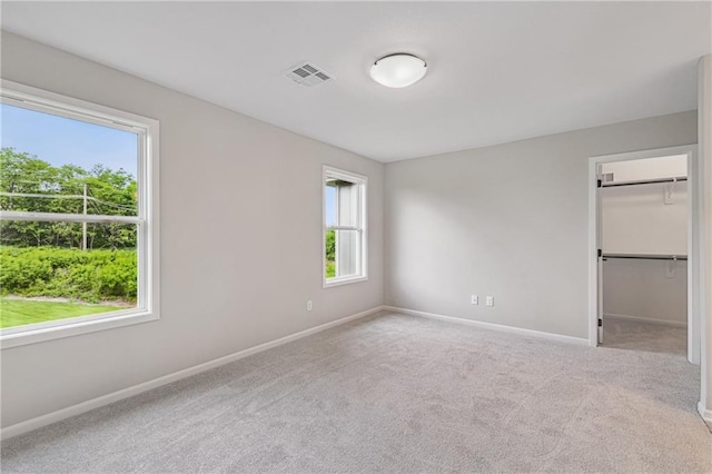 unfurnished bedroom featuring carpet floors, baseboards, visible vents, and a walk in closet