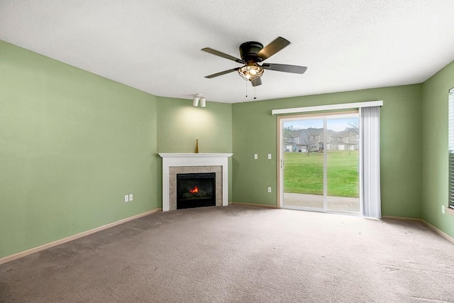 unfurnished living room with ceiling fan, carpet floors, a tiled fireplace, and baseboards