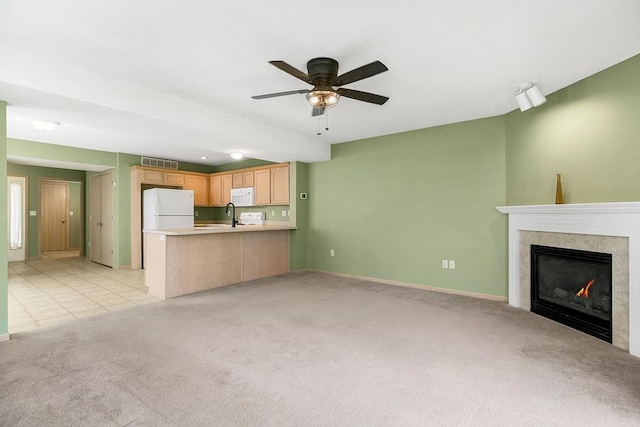 unfurnished living room with ceiling fan, light carpet, visible vents, baseboards, and a tiled fireplace