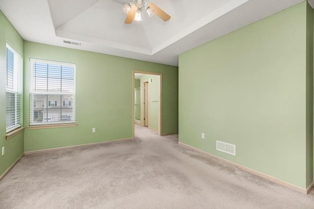 carpeted spare room featuring ceiling fan, a raised ceiling, visible vents, and baseboards