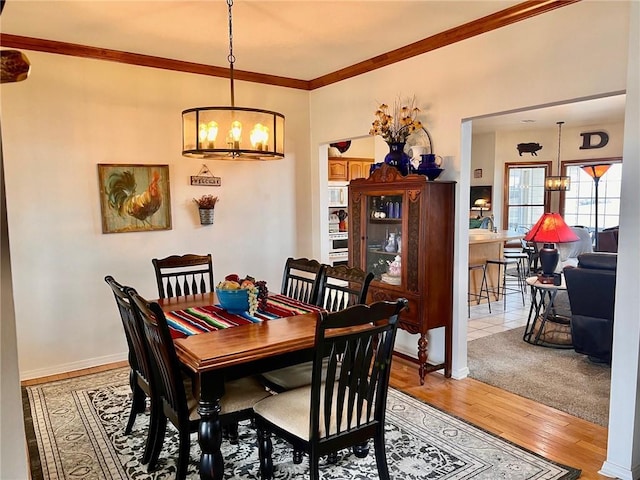 dining space featuring light wood-style floors, baseboards, ornamental molding, and a notable chandelier