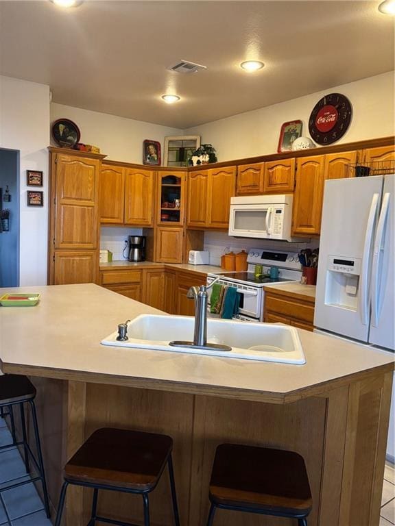 kitchen with white appliances, light tile patterned floors, brown cabinetry, and a sink