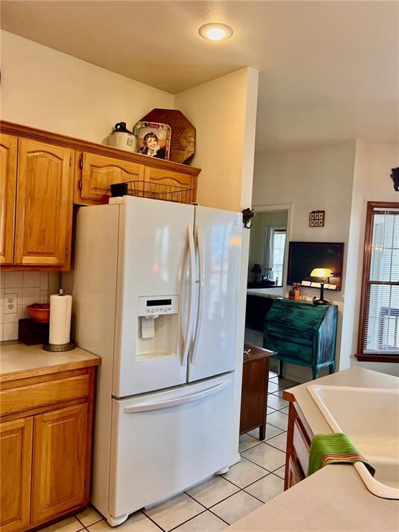 kitchen featuring brown cabinets, white refrigerator with ice dispenser, light tile patterned flooring, and decorative backsplash