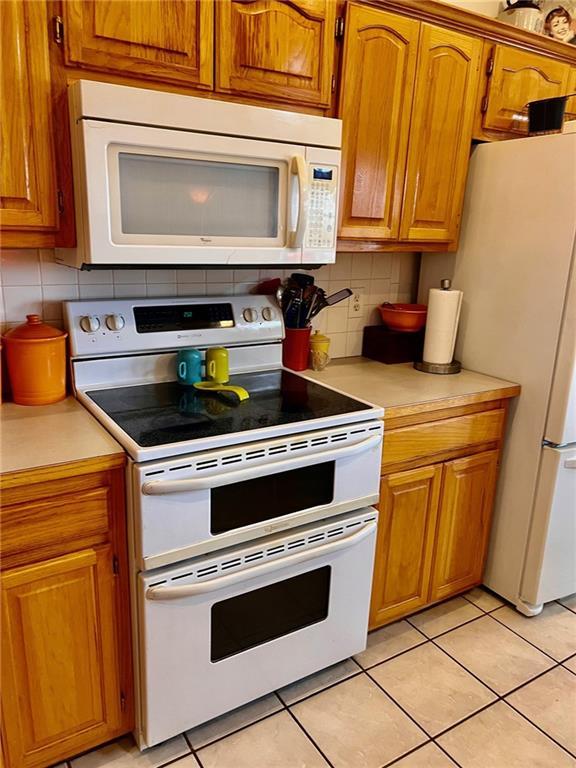 kitchen with white appliances, light tile patterned floors, brown cabinetry, light countertops, and backsplash