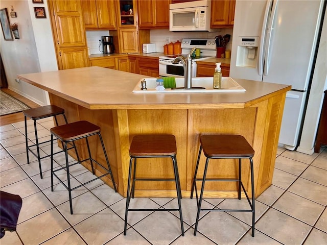 kitchen featuring white appliances, light tile patterned floors, brown cabinets, a breakfast bar, and light countertops