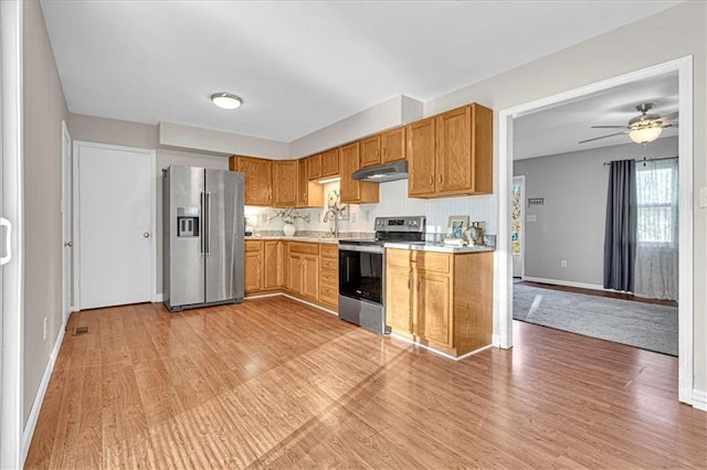 kitchen with light wood finished floors, baseboards, under cabinet range hood, light countertops, and appliances with stainless steel finishes