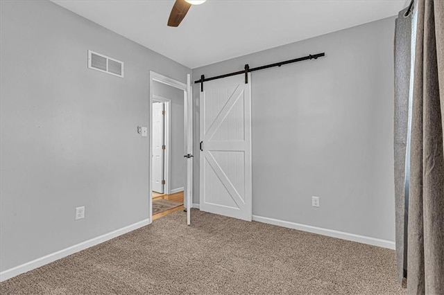 carpeted empty room with a barn door, baseboards, visible vents, and ceiling fan