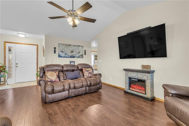 living area featuring a stone fireplace, wood finished floors, a ceiling fan, baseboards, and vaulted ceiling