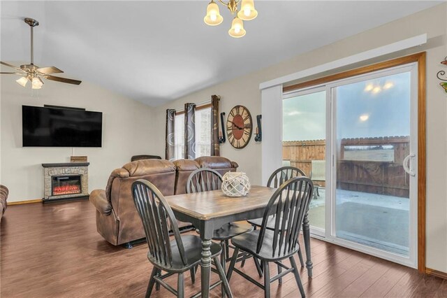 dining room with ceiling fan with notable chandelier, a fireplace, baseboards, vaulted ceiling, and dark wood finished floors