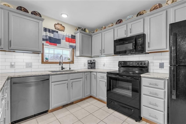 kitchen with light tile patterned floors, gray cabinetry, a sink, backsplash, and black appliances