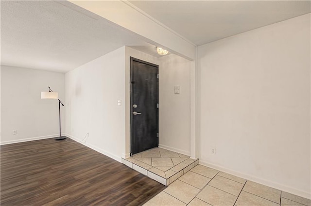 unfurnished room with a textured ceiling, wood finished floors, and baseboards