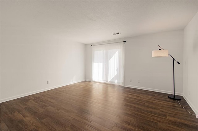 empty room with dark wood-style floors, visible vents, a textured ceiling, and baseboards