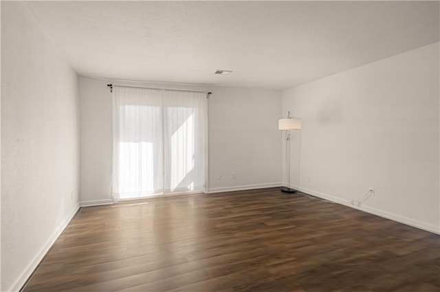 unfurnished room with dark wood-style floors, baseboards, visible vents, and a textured ceiling