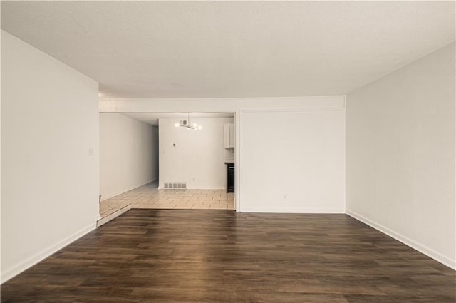 empty room with baseboards, visible vents, a chandelier, and wood finished floors