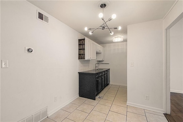 kitchen featuring light tile patterned floors, tasteful backsplash, visible vents, white cabinetry, and a sink