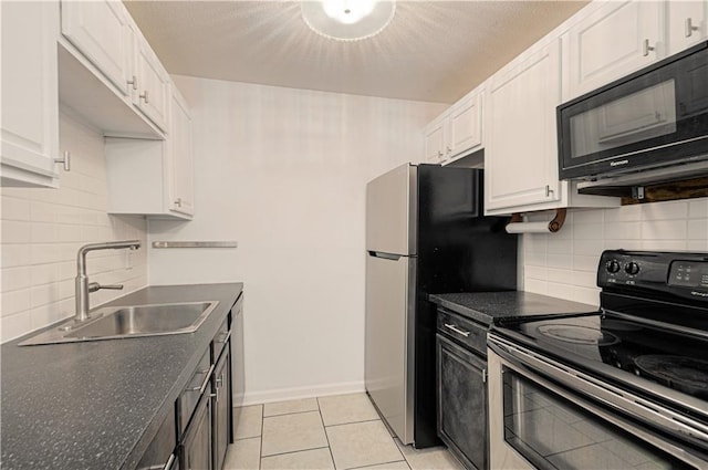 kitchen featuring light tile patterned floors, dark countertops, appliances with stainless steel finishes, white cabinetry, and a sink