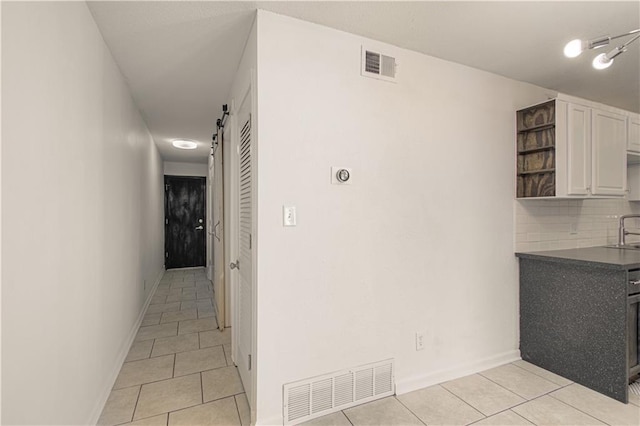 hall featuring light tile patterned floors, a barn door, and visible vents