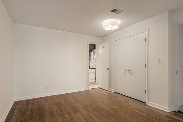 unfurnished bedroom featuring baseboards, a closet, visible vents, and wood finished floors