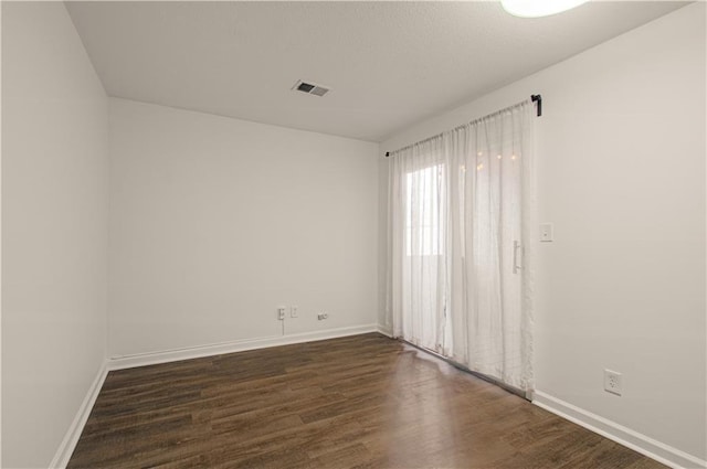 empty room featuring a textured ceiling, dark wood finished floors, visible vents, and baseboards