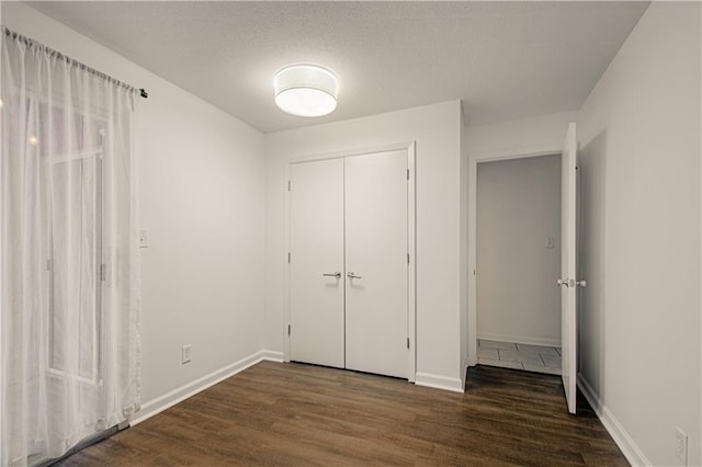 unfurnished bedroom with a closet, a textured ceiling, baseboards, and wood finished floors