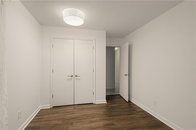 unfurnished bedroom with a closet, a textured ceiling, baseboards, and dark wood-style flooring