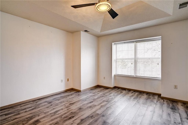 empty room with visible vents, a raised ceiling, baseboards, and wood finished floors