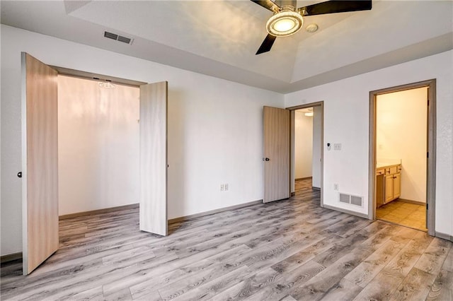 unfurnished bedroom featuring visible vents, a raised ceiling, light wood-style floors, and baseboards