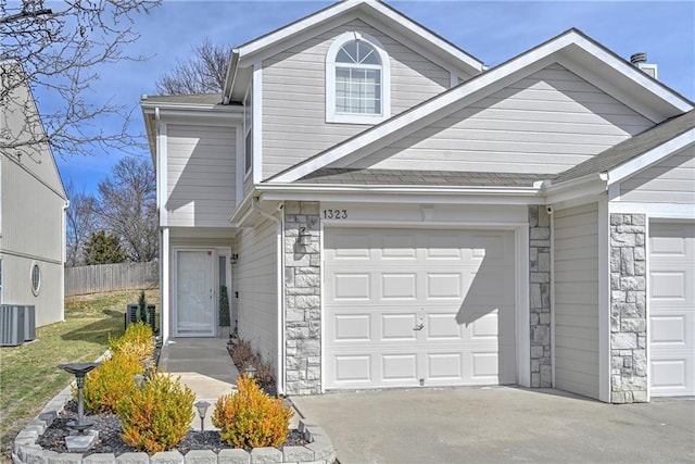 view of front of home with driveway, stone siding, central AC, fence, and an attached garage