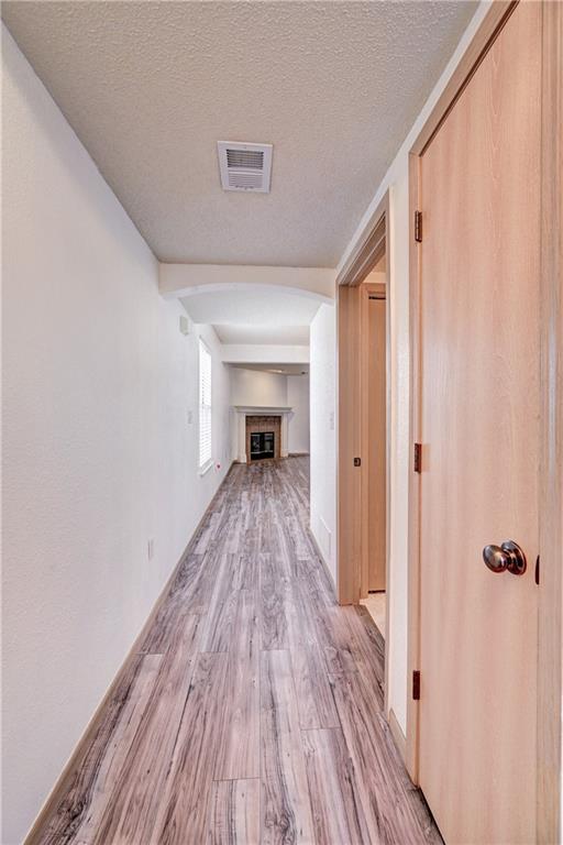 corridor featuring visible vents, a textured ceiling, and light wood finished floors