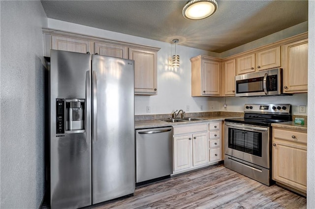 kitchen featuring light brown cabinets, appliances with stainless steel finishes, light wood-type flooring, and a sink