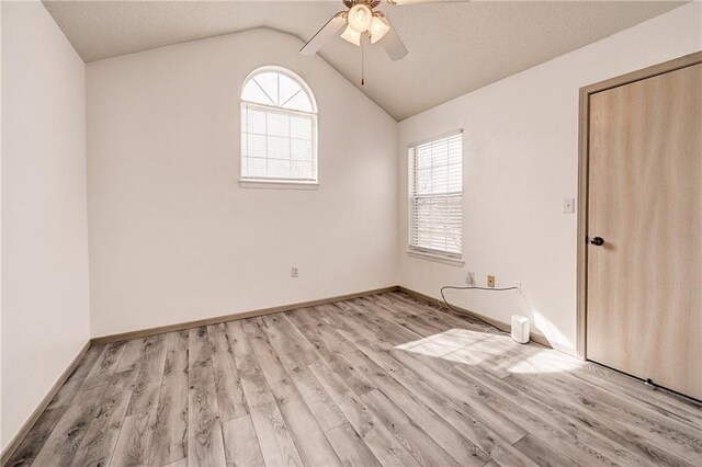 unfurnished bedroom with baseboards, multiple windows, lofted ceiling, and light wood-style flooring