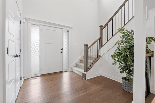 entrance foyer with baseboards, stairs, a towering ceiling, and hardwood / wood-style floors