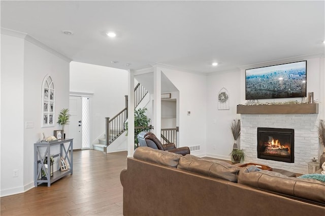 living room with a brick fireplace, crown molding, baseboards, stairway, and wood finished floors