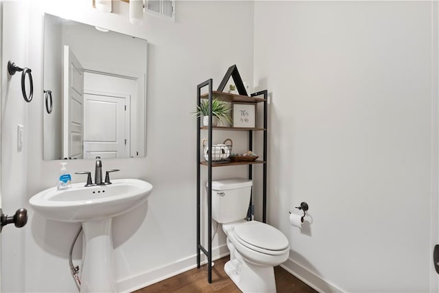 half bathroom with visible vents, baseboards, toilet, wood finished floors, and a sink