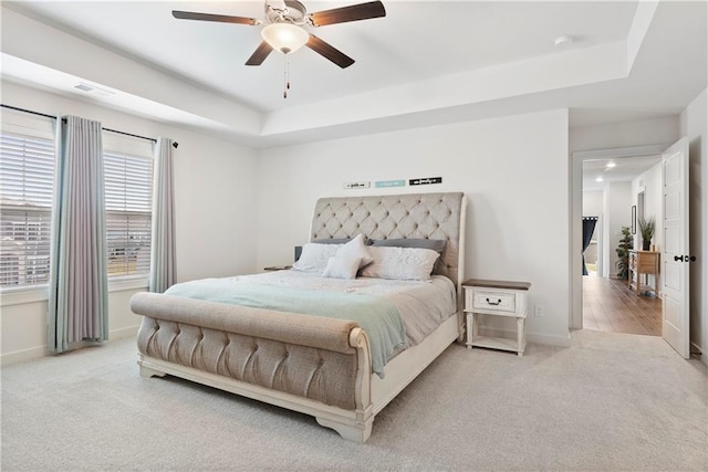 carpeted bedroom featuring a raised ceiling, visible vents, baseboards, and ceiling fan