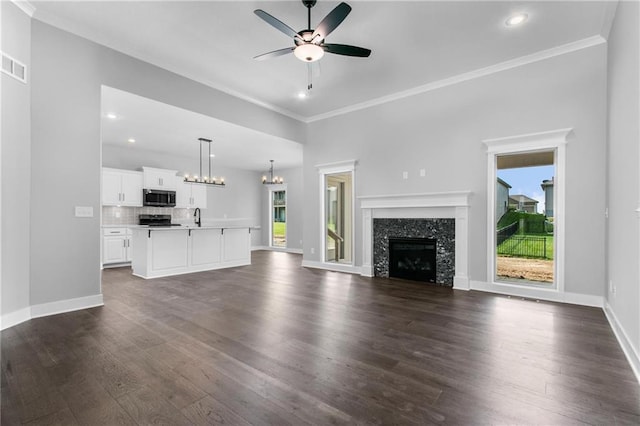 unfurnished living room with a fireplace, dark wood finished floors, ornamental molding, baseboards, and ceiling fan with notable chandelier