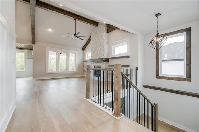 hall featuring beam ceiling, baseboards, an upstairs landing, and wood finished floors