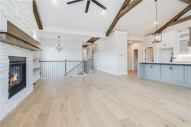 unfurnished living room featuring lofted ceiling with beams, a stone fireplace, light wood-style flooring, ceiling fan with notable chandelier, and a sink