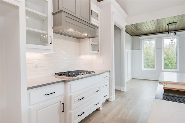 kitchen with stainless steel gas cooktop, light countertops, custom exhaust hood, and glass insert cabinets