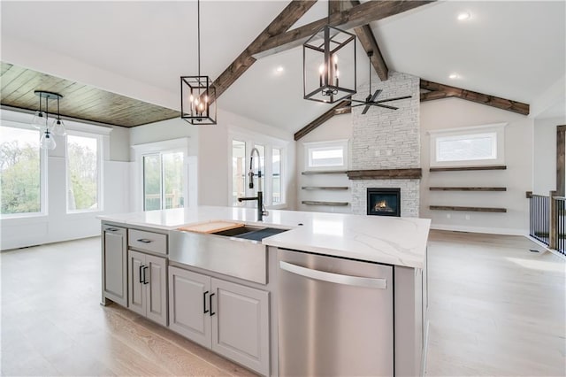 kitchen with lofted ceiling with beams, open floor plan, a kitchen island with sink, stainless steel dishwasher, and a sink