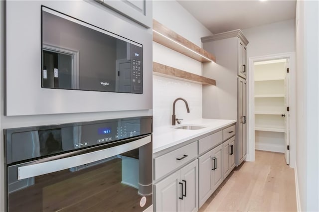 kitchen with black microwave, oven, a sink, light wood-type flooring, and open shelves