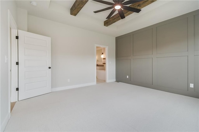 unfurnished bedroom featuring light carpet, baseboards, ensuite bath, ceiling fan, and beam ceiling