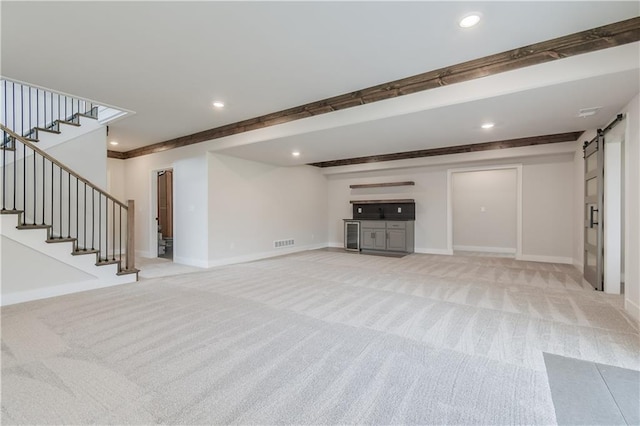 unfurnished living room with a barn door, light carpet, visible vents, baseboards, and stairway