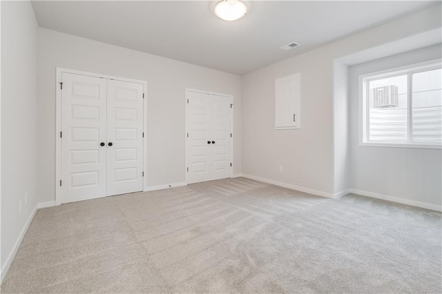 unfurnished bedroom featuring light colored carpet, visible vents, baseboards, and two closets