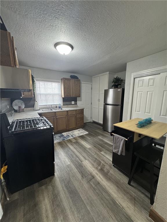 kitchen featuring dark wood-style flooring, gas range oven, light countertops, freestanding refrigerator, and a textured ceiling