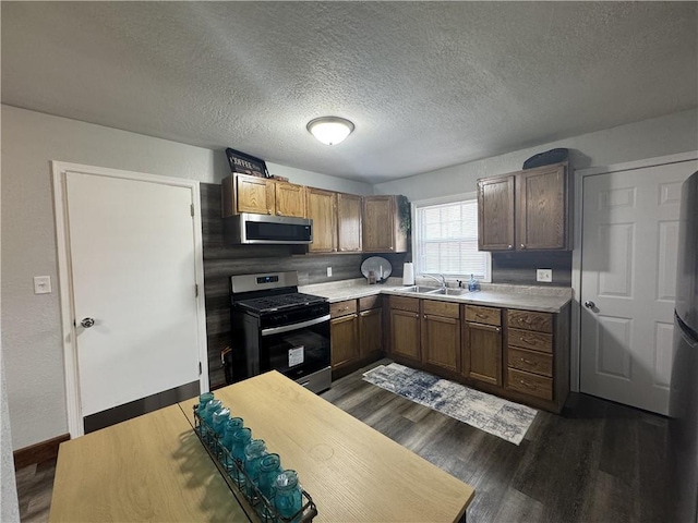 kitchen with light countertops, appliances with stainless steel finishes, dark wood-type flooring, and a sink