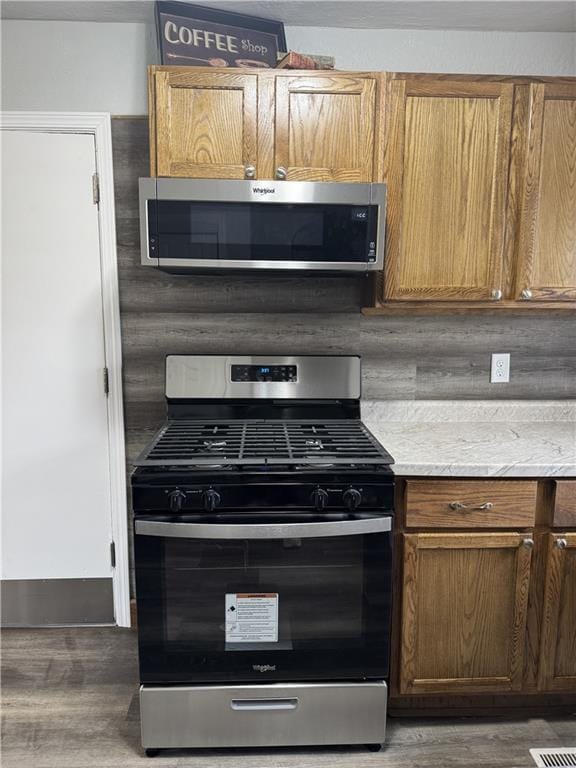 10904 Cambridge Ave, Kansas City, MO 64134 - kitchen featuring stainless steel appliances, light stone counters, decorative backsplash, and wood finished floors