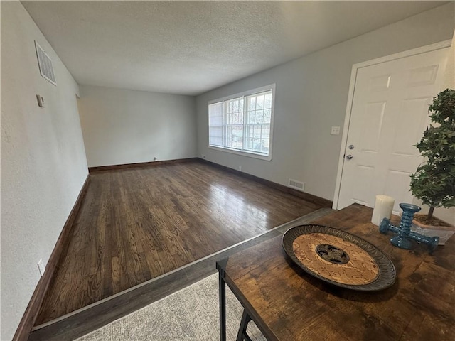 10904 Cambridge Ave, Kansas City, MO 64134 - unfurnished living room with visible vents, a textured ceiling, baseboards, and wood finished floors